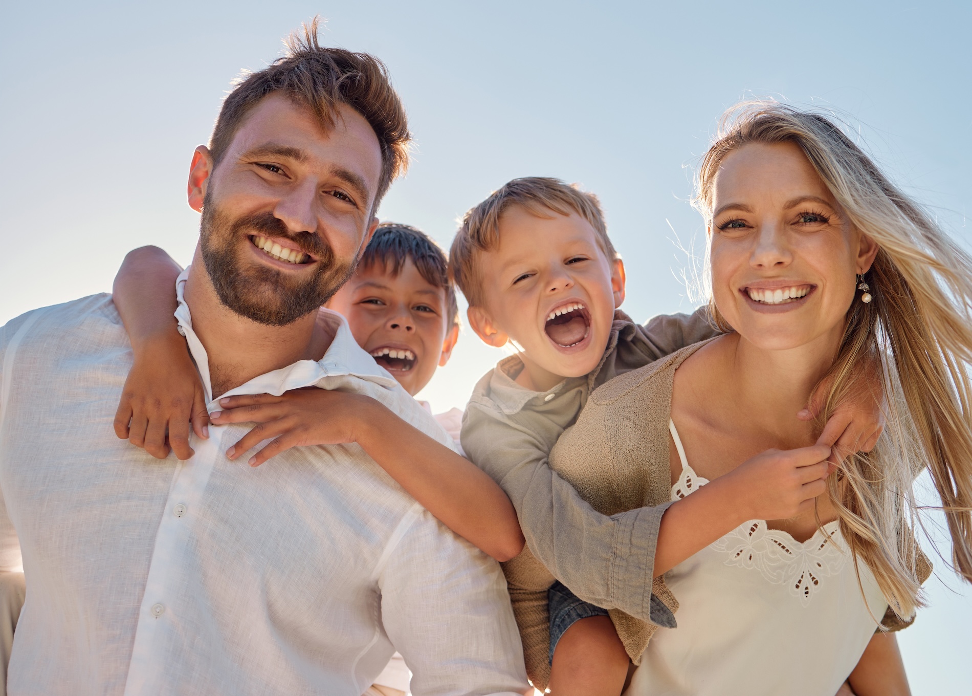 En smilende familie nyder en solskinsdag på stranden med to børn på deres skuldre.