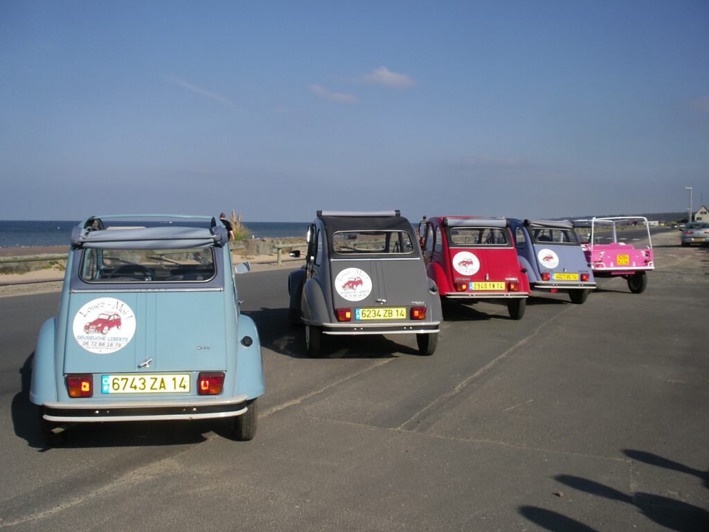 Fem vintage biler parkeret på havet med udsigt over stranden og en klar himmel.