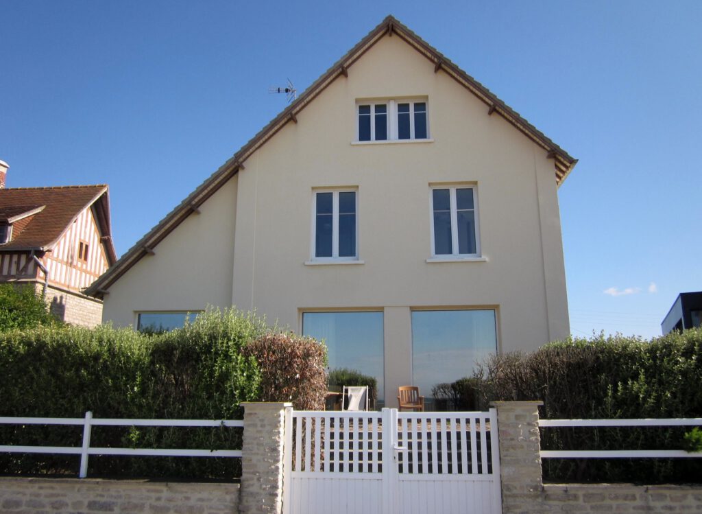Fasade af et moderne hus på stranden med store vinduer og have, der ligger i Asnelles, Normandiet.