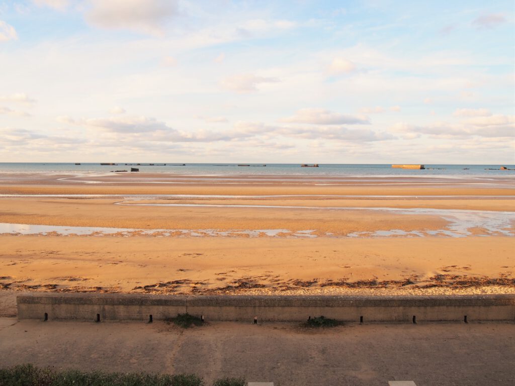 Asnelles Beach, med gyldent sand og rolige farvande, der tilbyder udsigt over offshore historiske strukturer.