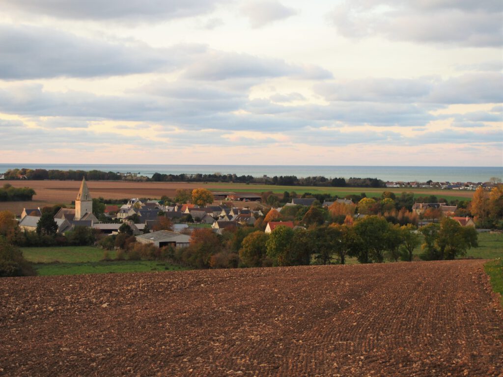 Panoramaudsigt over Norman -landsbyen Asnelles med sin kirke, omgivet af marker og havet i det fjerne.