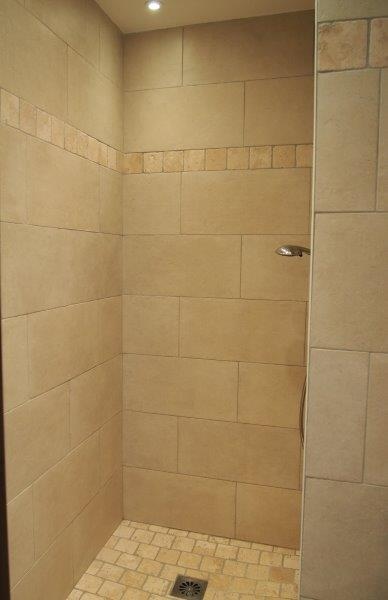 Moderne brusebad i fliser, beige fajancevægge og mosaikgulve, blød belysning.