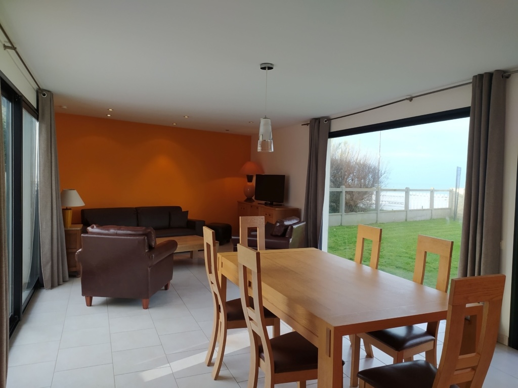 Interiør af et sommerhus ved havet i Asnelles, med stue, spisestue og udsigt over haven og havet.