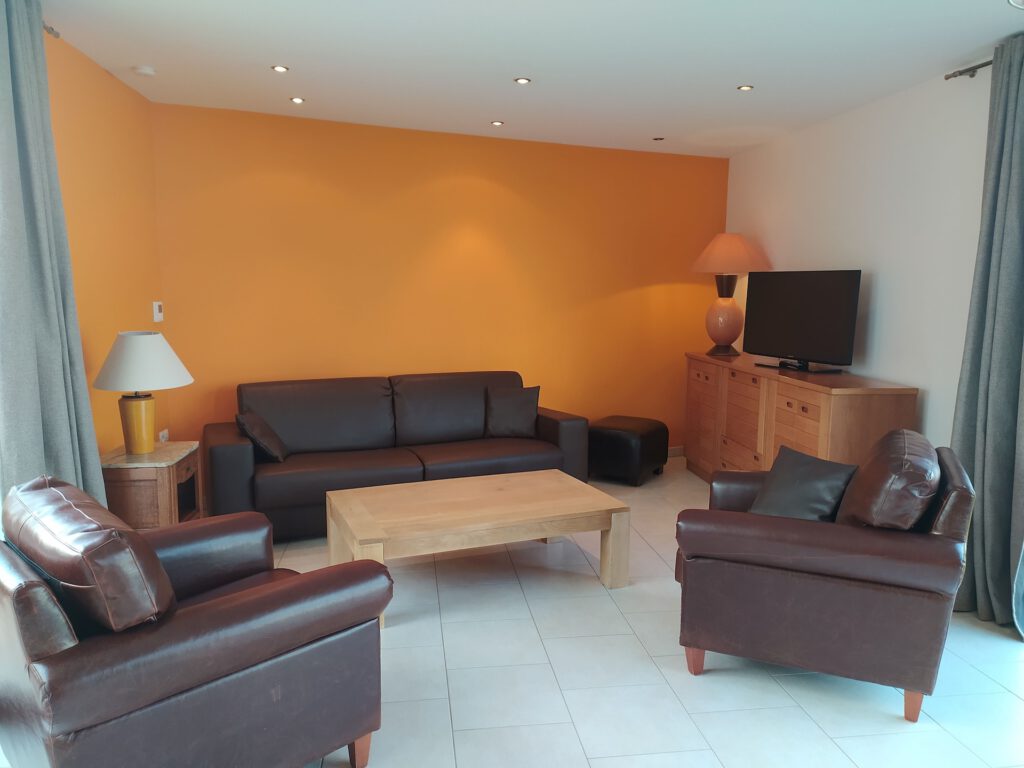 Moderne stue med lædersofa, lænestole, træbord og tv på orange baggrund.